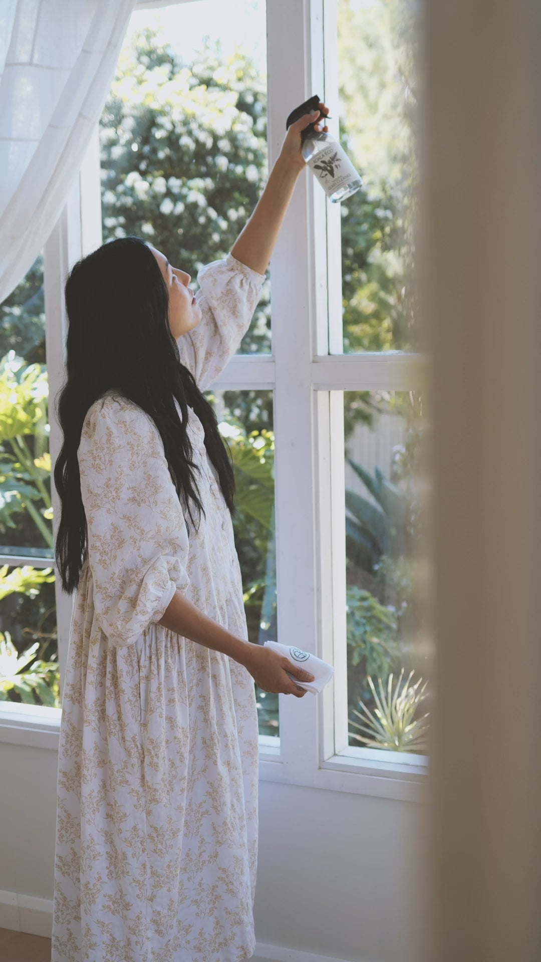 A woman cleaning a window with Koala Eco's glass cleaner